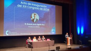 Escenario con una mesa de participantes y una persona hablando ante un atril.