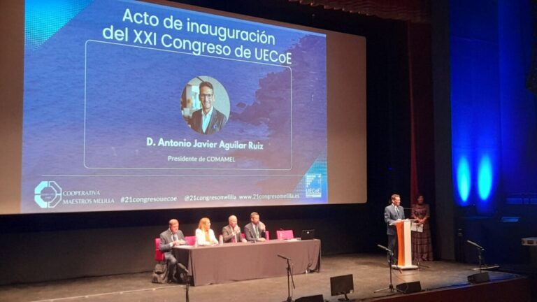 Escenario con una mesa de participantes y una persona hablando ante un atril.