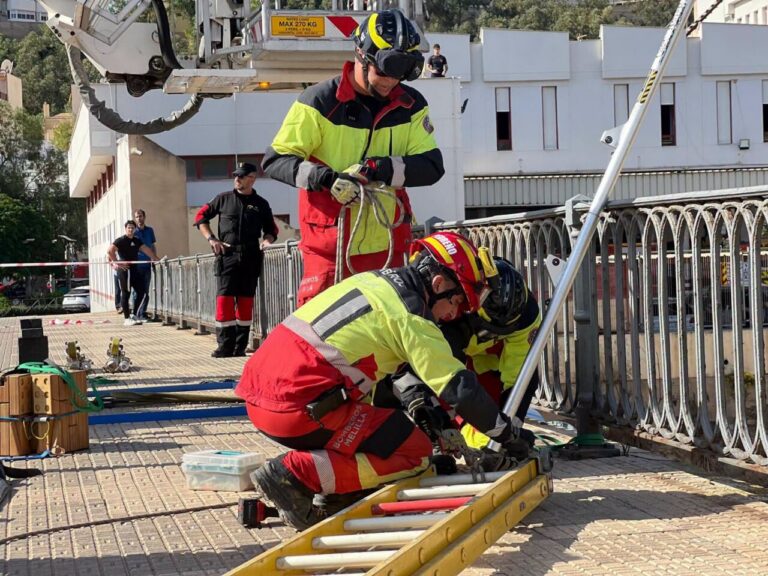 Bomberos con equipo de rescate y cuerdas realizan una práctica junto a una escalera.