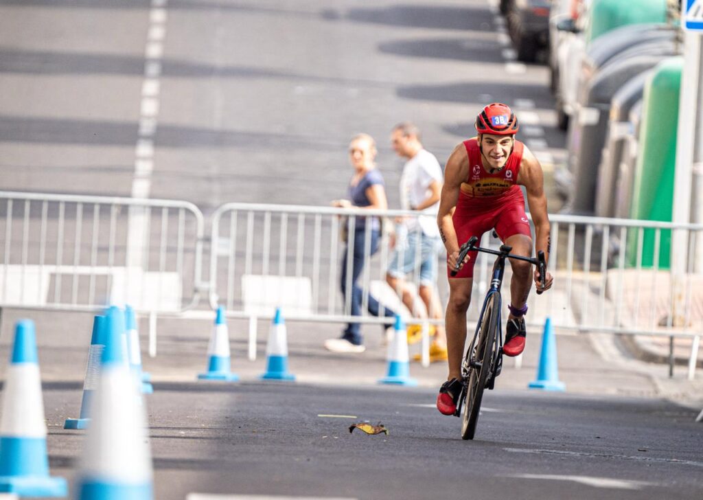 Un ciclista con uniforme rojo pedalea entre conos en un circuito urbano.
