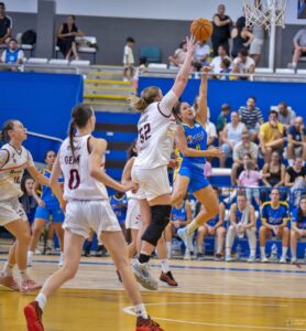 Women’s basketball game: two players jump for the ball near the basket as teammates and spectators watch.