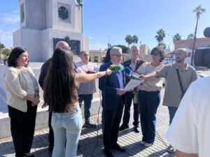 Un hombre lee un documento ante varios micrófonos mientras periodistas lo rodean al aire libre.