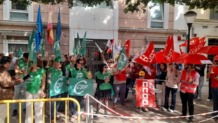 Personas se concentran frente a un edificio con banderas y pancartas sindicales.