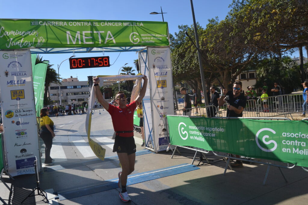 Un corredor levanta la cinta bajo el arco de meta de la carrera en Melilla.
