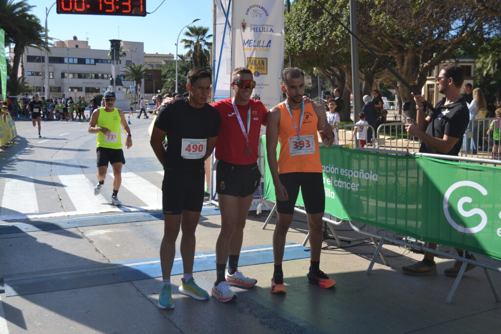 Tres corredores con dorsales posan en la meta mientras otro participante se acerca.