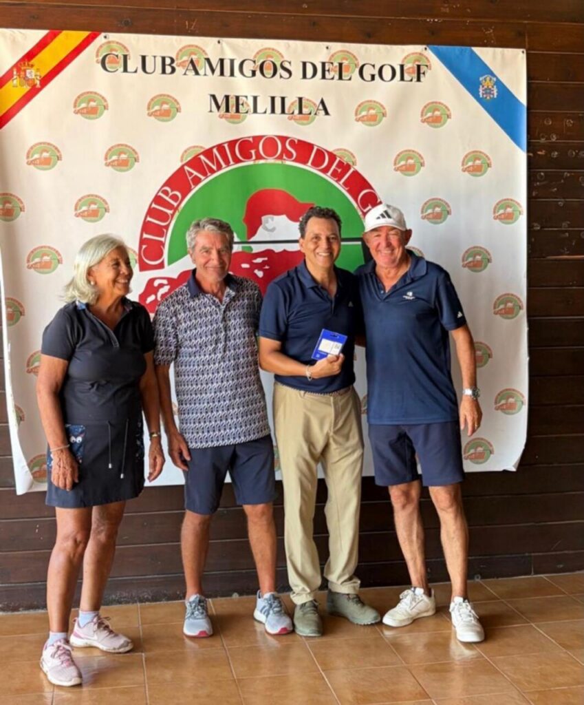 Four adults posing for a photo at Club Amigos del Golf Melilla, with a banner in the background and one man displaying a small blue award box.