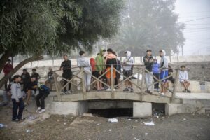 Group of teenagers on a wooden footbridge, talking and hanging out, in a misty park setting under trees.