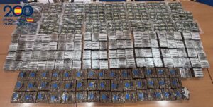 Large quantity of rectangular packages arranged on a table, police logo present, likely seized drugs.