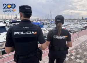Dos agentes de la Policía Nacional junto a embarcaciones amarradas en un puerto deportivo.