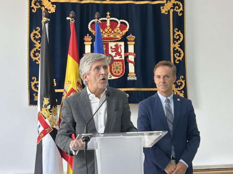 Dos hombres junto a un atril durante una comparecencia con banderas al fondo