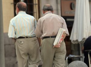 Dos hombres caminan de espaldas y uno lleva un periódico doblado bajo el brazo.