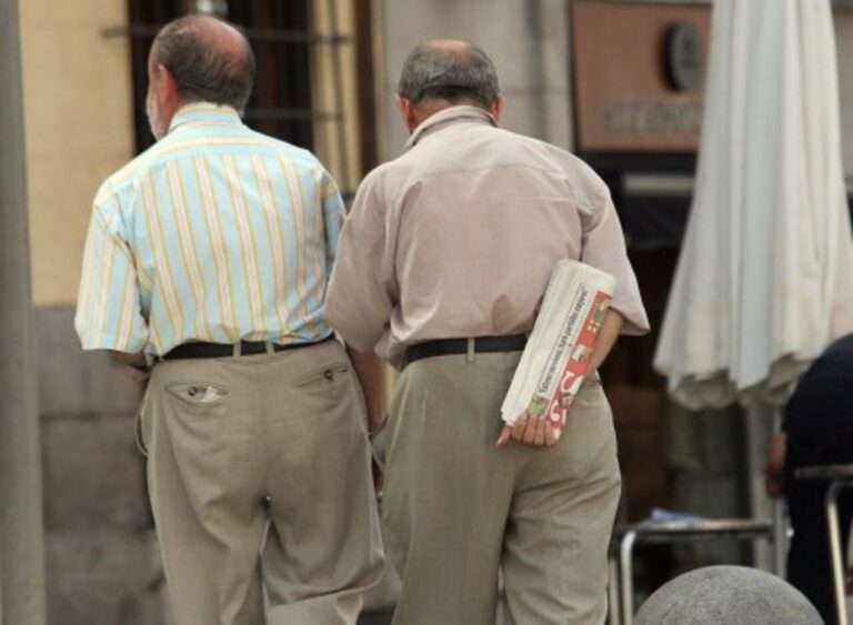 Dos hombres caminan de espaldas y uno lleva un periódico doblado bajo el brazo.