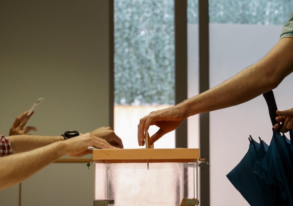 Manos depositando votos en una urna electoral durante elecciones