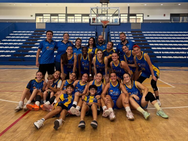 Grupo de jugadoras y acompañantes posa en una cancha de baloncesto bajo la canasta.