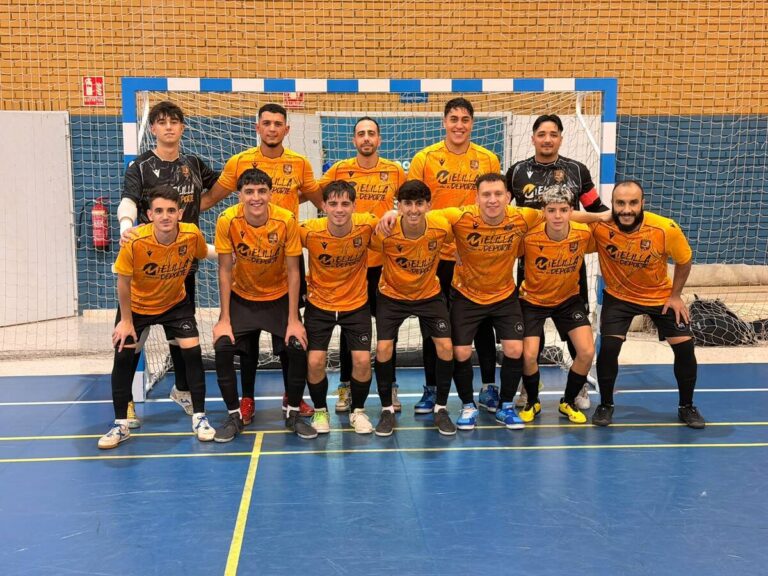 Eleven-player futsal team in orange jerseys posing in front of a goal on an indoor blue court.