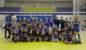 Jugadoras de voleibol, menores y mascotas posan juntas en una cancha.