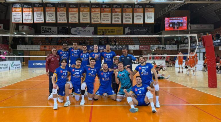 Equipo de voleibol con uniforme azul posa en la cancha junto a la red