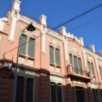 Fachada ornamentada de la Cámara de Comercio, con balcones y cables bajo cielo azul.