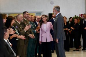 Woman in a pink blazer greets a line of uniformed military officers and officials at a formal event with applause around.