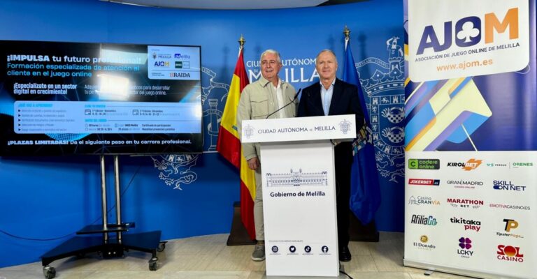 Dos hombres junto a un atril de Melilla, con pantallas y cartel de AJOM
