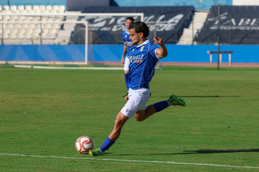 Futbolista con uniforme azul de Melilla golpea el balón sobre el césped.