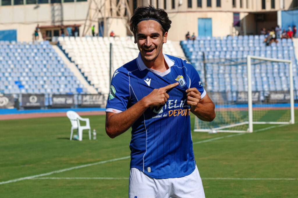 Futbolista con uniforme azul señala el escudo de su camiseta en el campo