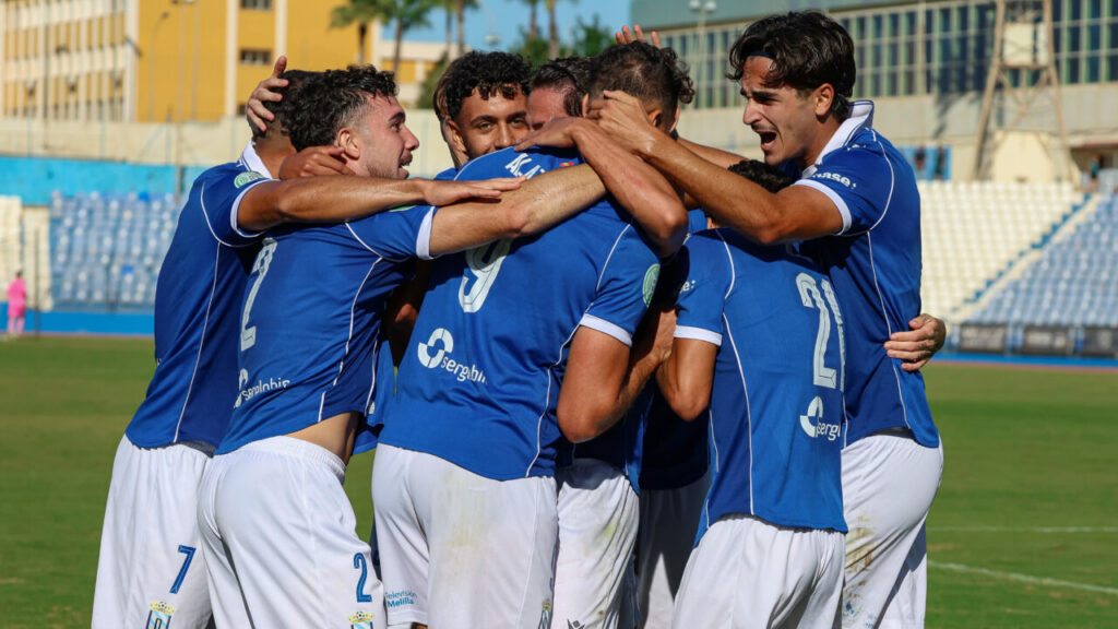 Futbolistas con camisetas azules se abrazan en grupo sobre el césped.