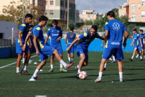 A group of soccer players in blue uniforms practice ball control on a turf field during a training session.