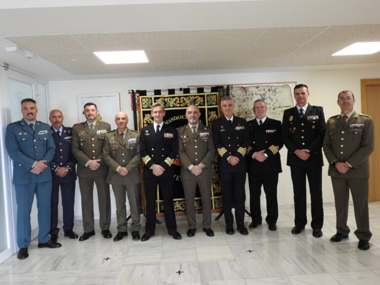 Grupo de hombres uniformados posa en una sala junto a un estandarte decorado.