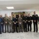 Grupo de hombres uniformados posa en una sala junto a un estandarte decorado.