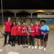 Ocho personas posan de noche con medallas y varios trofeos, algunas con camisetas rojas.