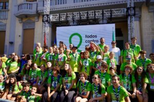 Grupo de participantes con camisetas verdes posa ante un cartel de lucha contra el cáncer.