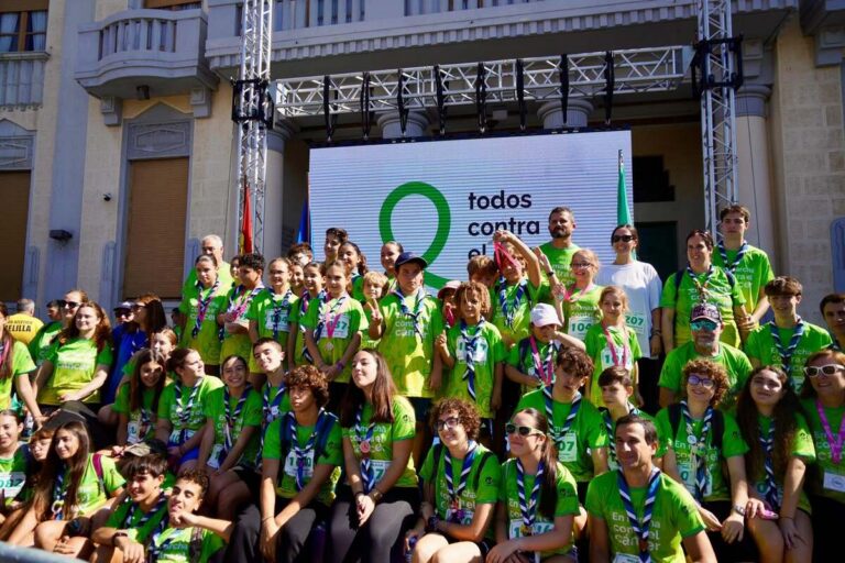 Grupo de participantes con camisetas verdes posa ante un cartel de lucha contra el cáncer.