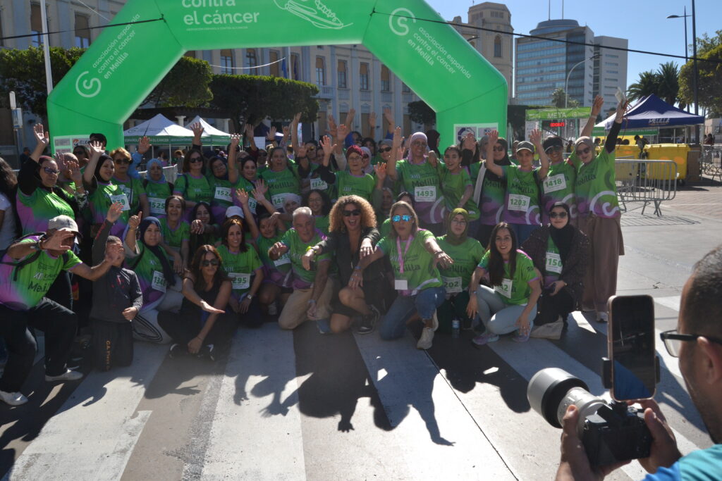 Grupo de participantes posa bajo el arco verde de una carrera contra el cáncer en Melilla.
