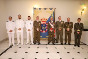 Ocho personas uniformadas posan en fila delante de un estandarte decorado.