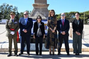 Seis personas posan frente a un monumento, con un militar uniformado a la izquierda.
