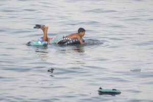 Un hombre se apoya sobre un flotador en el agua, con objetos dispersos alrededor.