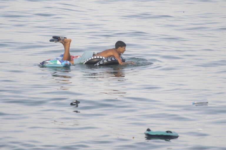Un hombre se apoya sobre un flotador en el agua, con objetos dispersos alrededor.