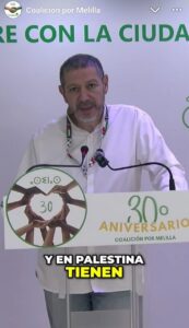 Hombre habla ante un atril de Coalición por Melilla con un cartel del 30 aniversario