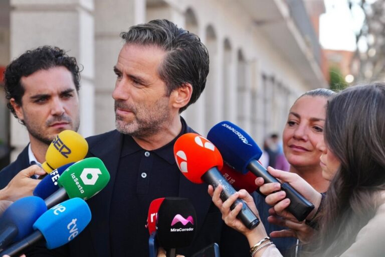 Un hombre habla ante varios micrófonos mientras otras personas lo rodean en la calle.