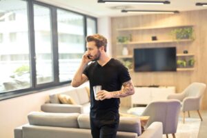 Hombre sostiene un teléfono junto al oído y un vaso en un salón