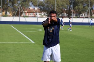 Hombre con ropa deportiva hace un gesto con los brazos en un campo de fútbol.