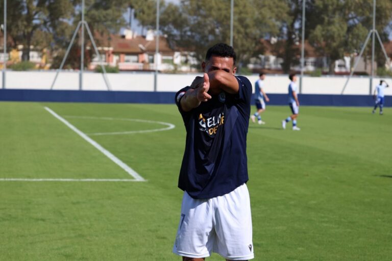 Hombre con ropa deportiva hace un gesto con los brazos en un campo de fútbol.