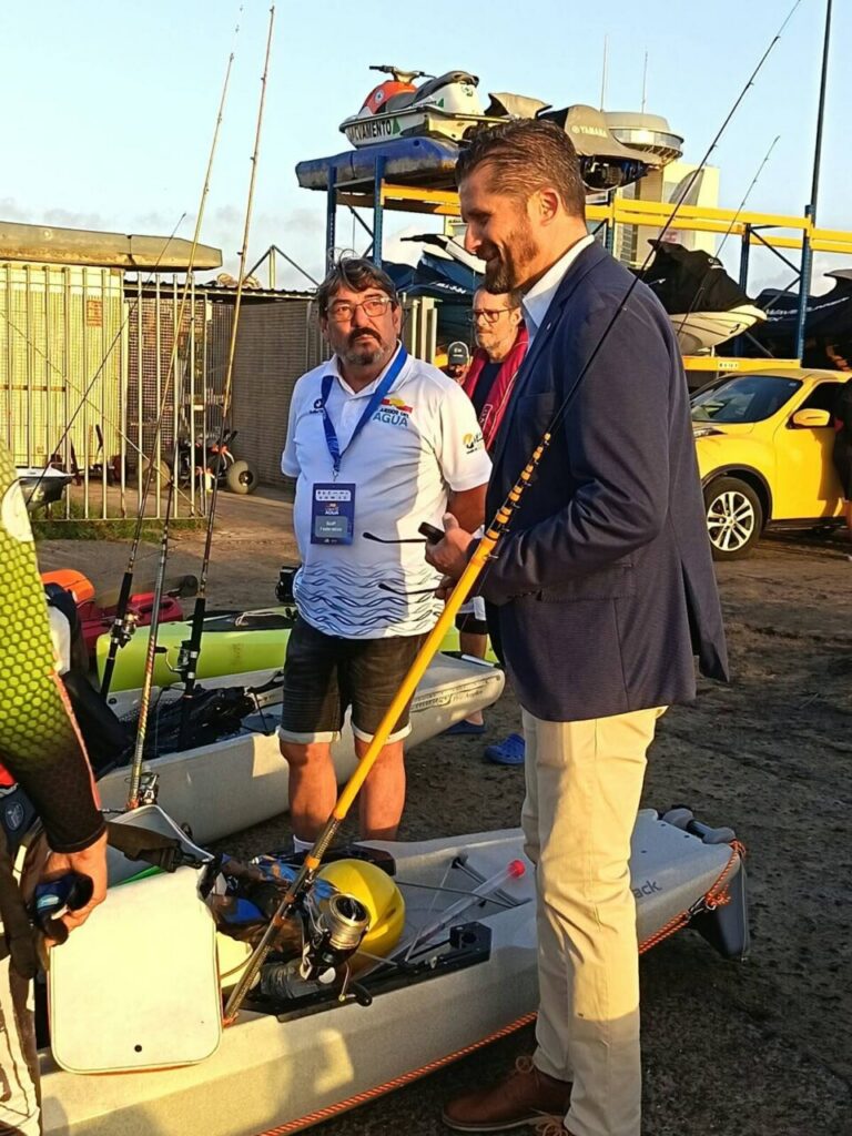 Dos hombres junto a kayaks y cañas de pescar en una zona de embarcaciones.