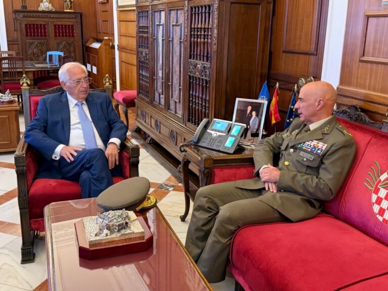 Dos hombres sentados frente a frente en un despacho de madera; uno viste uniforme militar.