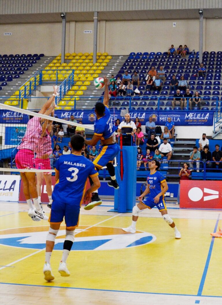Jugadores de voleibol saltan junto a la red mientras el balón cruza la cancha.