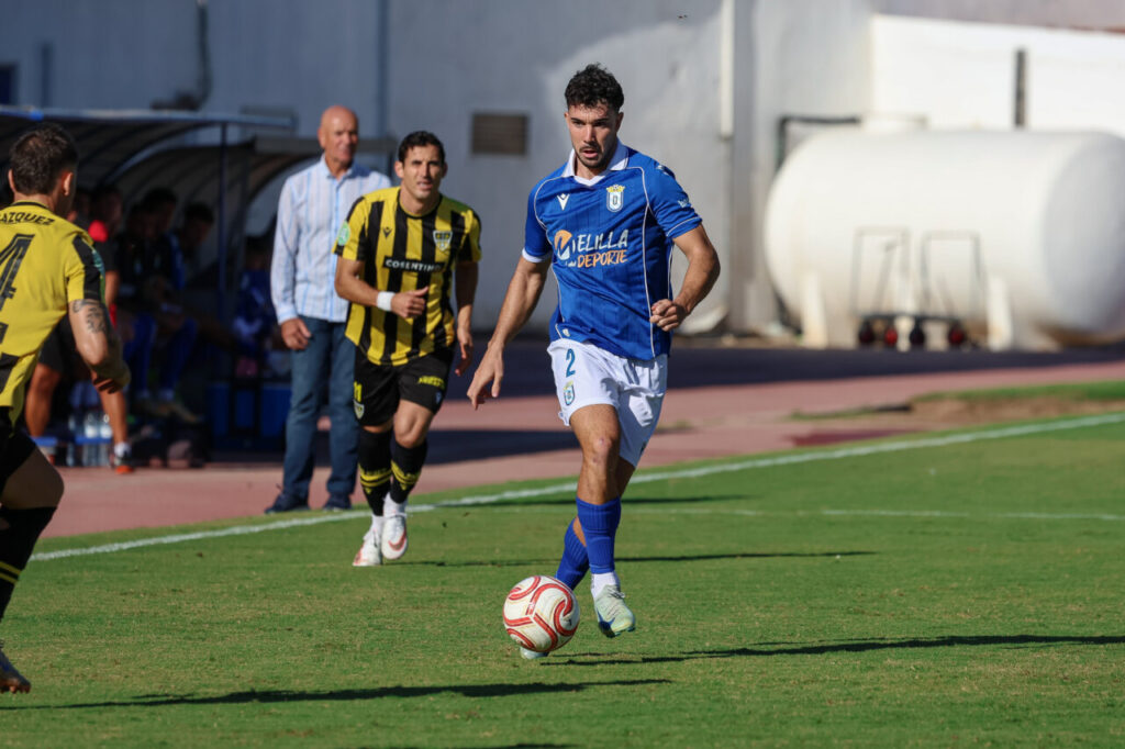 Fotografía de un futbolista de azul que conduce el balón ante dos rivales.