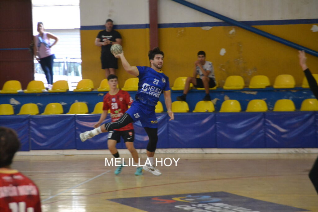 Jugador de balonmano con camiseta azul lanza el balón frente a un rival
