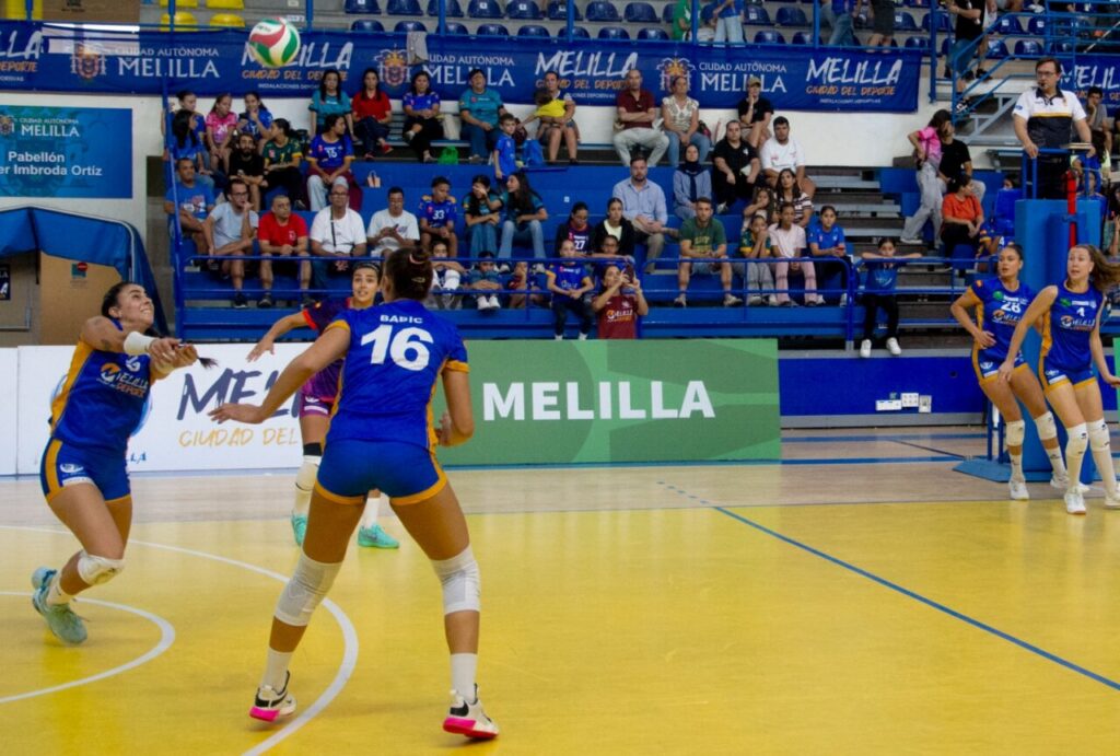 Jugadoras del Melilla disputan una jugada de voleibol ante espectadores en la grada.