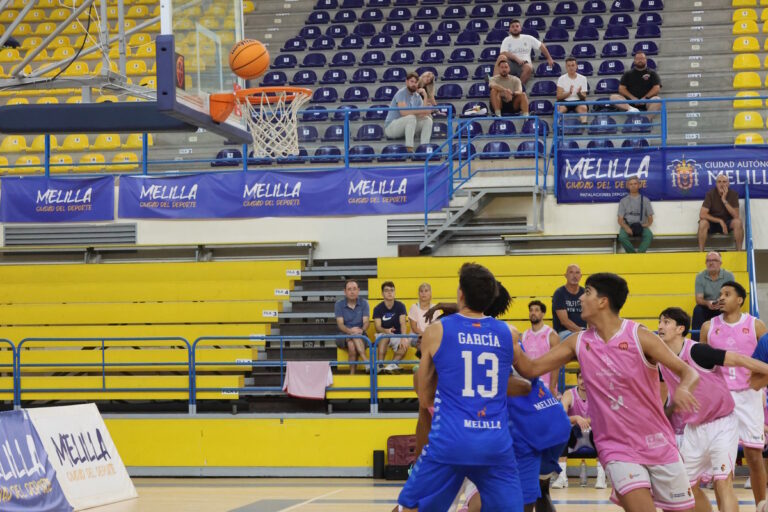 Jugadores de baloncesto en azul y rosa observan el balón junto a la canasta.